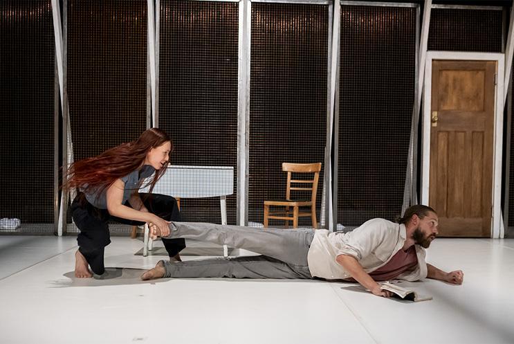 One performer lying on the ground. Another performers in crouched, pulling at the other performer's leg.