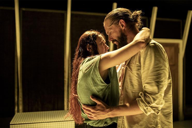 Two performers bathed in yellow light, embracing.. 