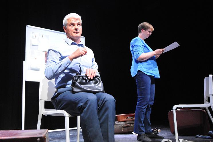 Two people on stage, on sitting and then other standing