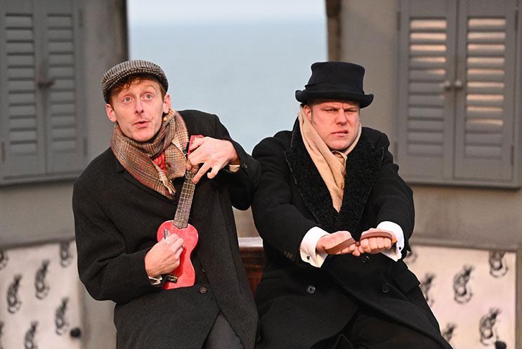 Two people dressed in large black overcoats. One person is holding a ukulele