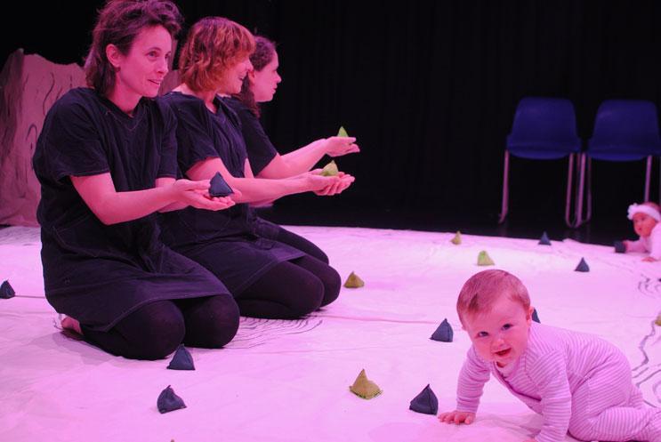 2 females kneeling on a white mat with a baby crawling