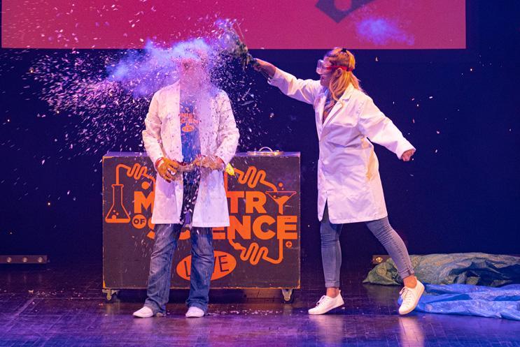 Two people dressed in lab coats and one of them is covering the other in something glittery.