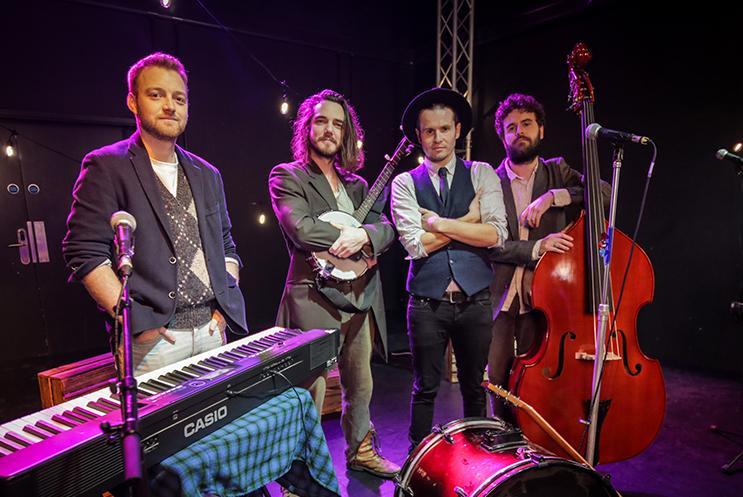 Fourmusicians standing together surrounded by instruments