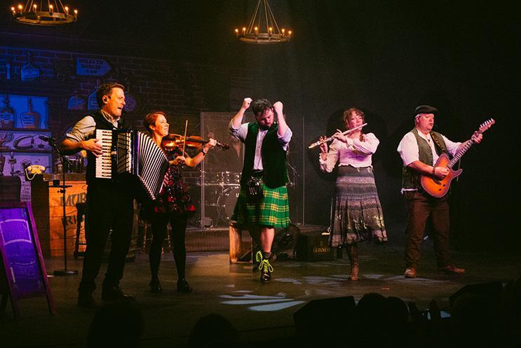 A group on stage dancing and playing instruments.