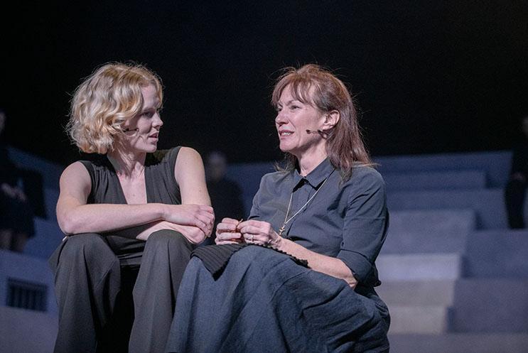 Two people dressed in grey sat talking to one another.