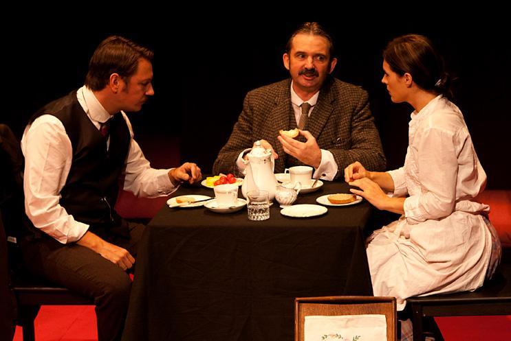 Three people sat around a table having tea in Victorian costume