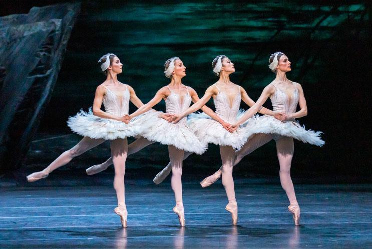 Four ballet dancer in a row performing and dressed in white.