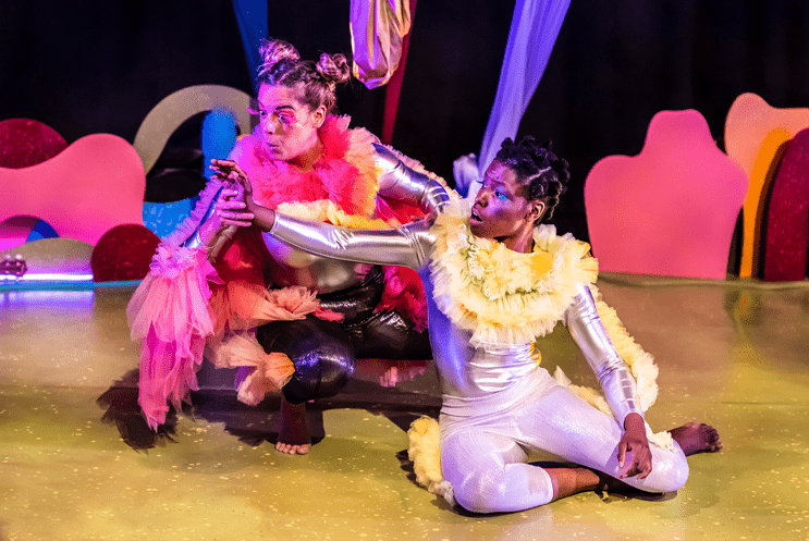 Two performer pointing dressed in yellow, siliver and pink costumes