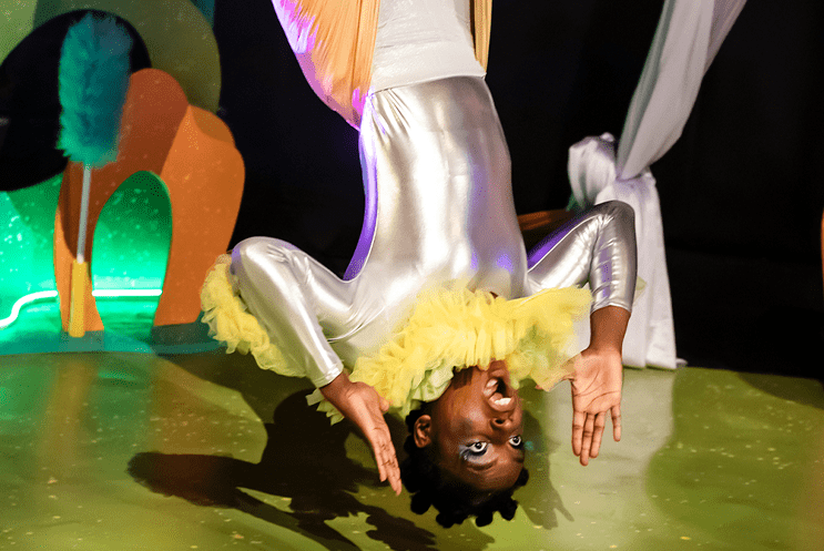 A performer dressed in yellow and silver hanging upside-down
