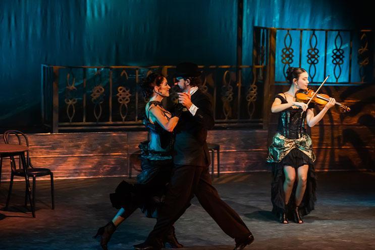 Two people ballroom dancing with a violinist in the background