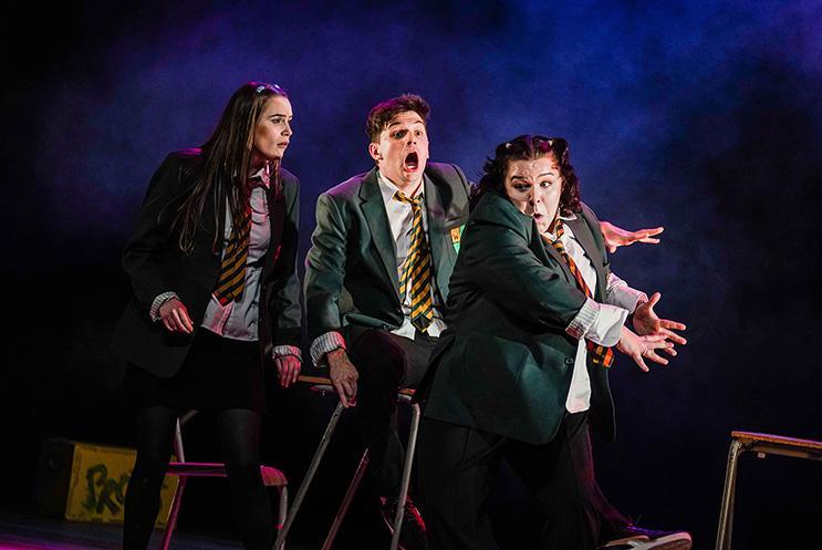 Three actors playing secondary school kids dressed in uniforms, playing around.
