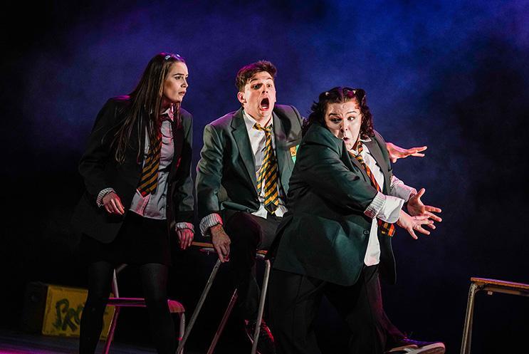 Three actors playing secondary school kids dressed in uniforms, playing around.