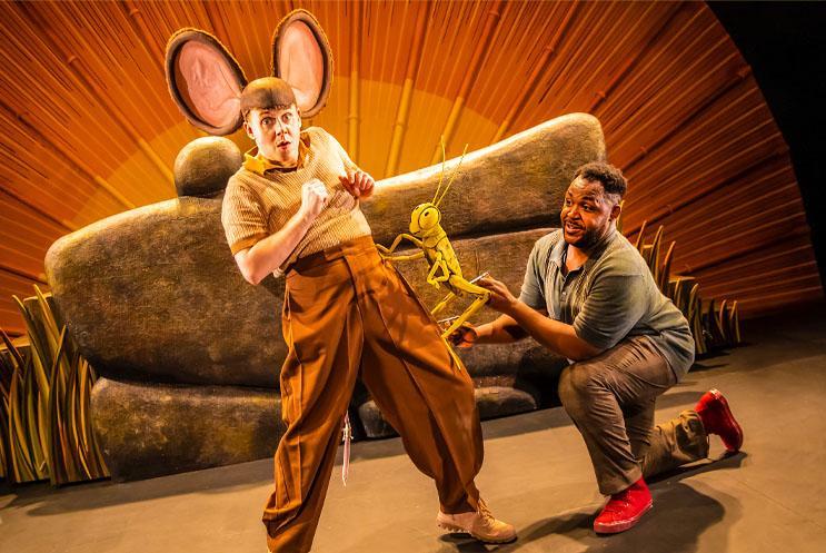 Performer dressed as a mouse with another performer puppeteering a cricket on his leg.