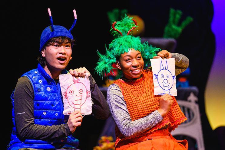Two people holding up drawings of aliens