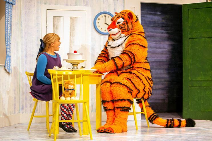 A person in a tiger costume sitting at a table and having tea with another person