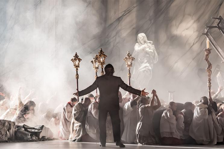 A man stood with his back to the audience, hand outstretched to a crowd of cowering people.