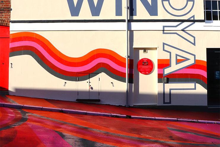 The artwork on the road and on the side of the theatre in shades of red, orange, pink and grey.