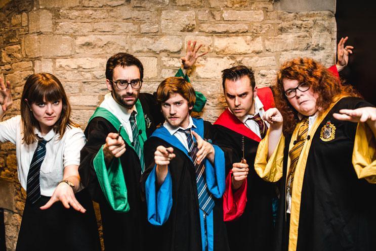 Five actors dressed as wizards casting a spell using wands looking at the camera
