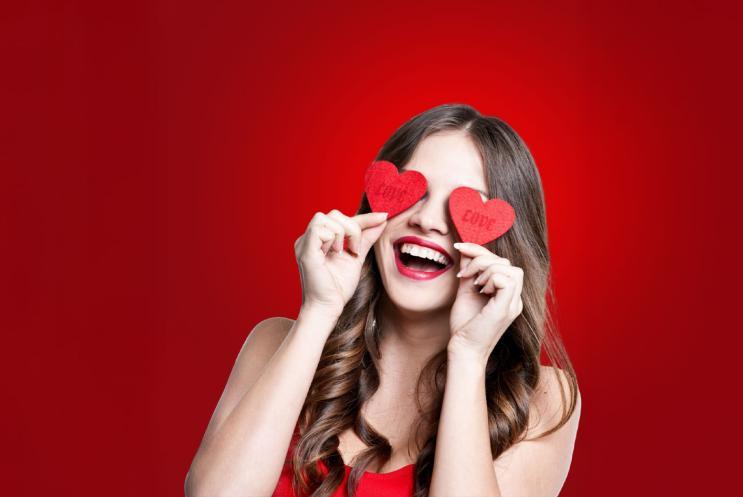 A person holding two paper love hearts over their eyes