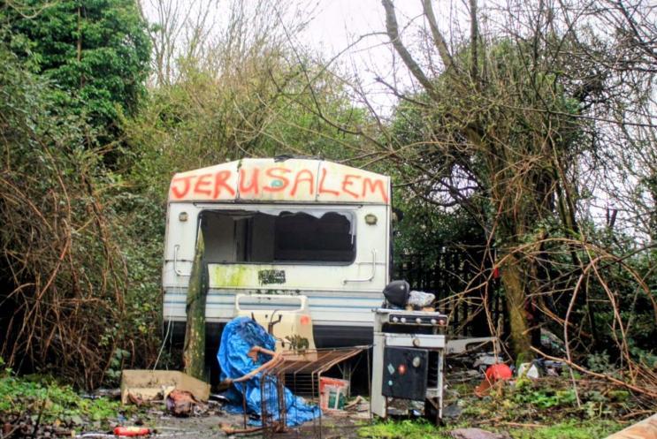 A beat-up-looking caravan surrounded by shrubbery with Jerusalem spray-painted on to it. 