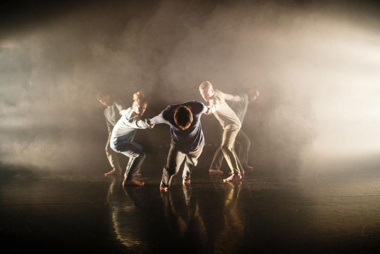 A group of male dancers performing on stage engulfed in haze and spotlights 