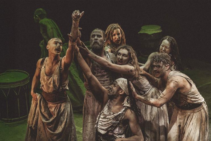 A group of people wearing robes, covered in clay and reaching up to the sky.