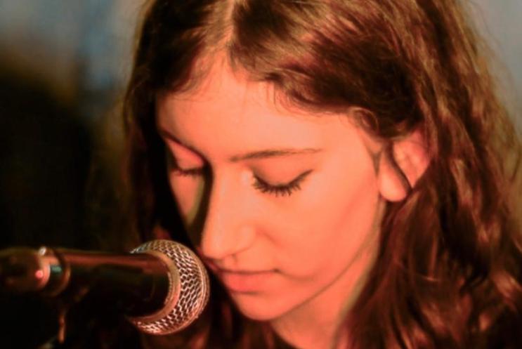 Headshot of woman with long brown hair looking down to microphone