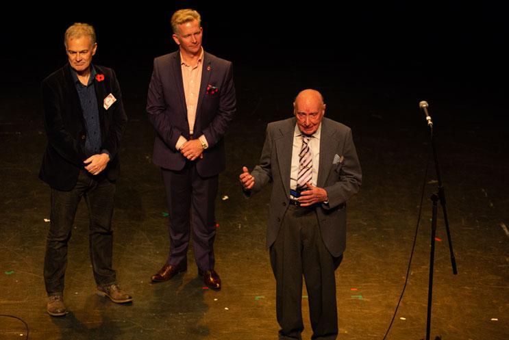 Three men stood on a stage in suits