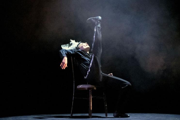 A dancer sitting in a chair and doing a high kick